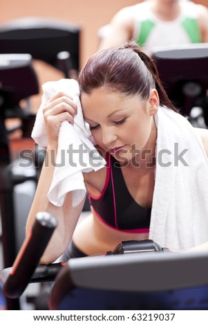 Exhausted woman wiping her face with a towel sitting on a cross trainer in a sport centre