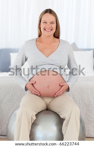 Front view of a happy future mom sitting on a fitness ball and looking at the camera