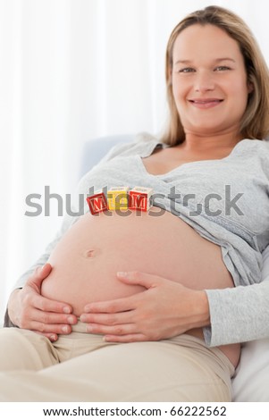 Side view of a happy woman with mom letters on the belly lying on a bed