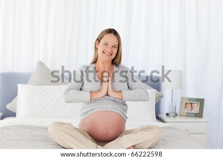Adorable future mom doing meditation sitting on the bed at home