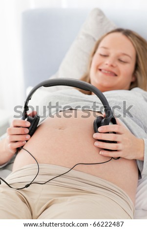 Happy pregnant woman putting headphones on her belly lying on a bed