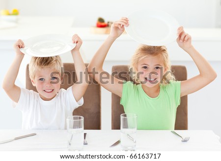 Funny brother and sister asking for their lunch raising their plates in the kitchen