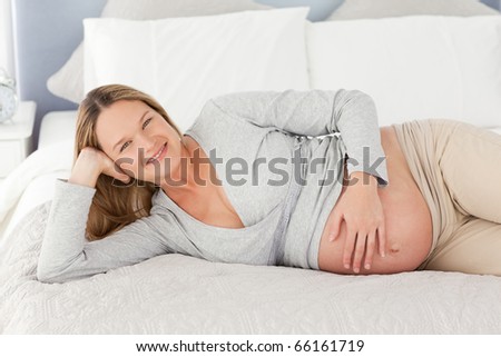 Happy future mom touching her belly on a bed