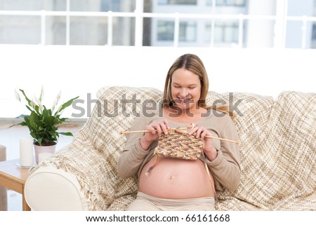 Happy pregnant woman knitting in the living-room at day