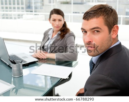 Serious businesspeople sitting around a table and looking at the camera in their office