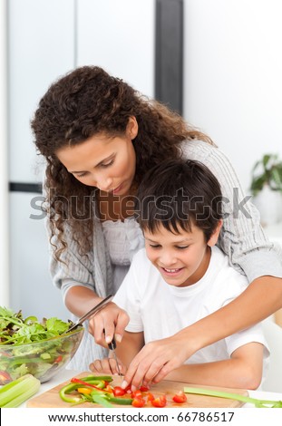 Attentive mother helping her son to cut vegetables in the kitchen