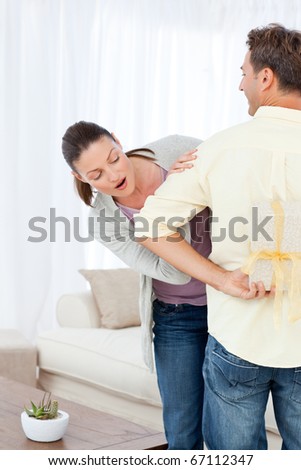 Impatient woman looking at a present hidden behing her boyfriend in the living room