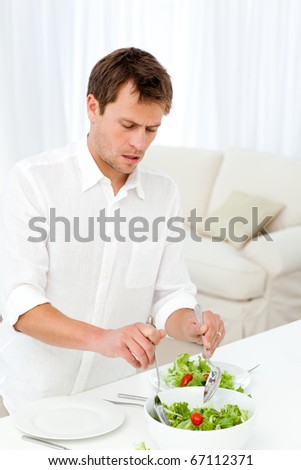 Single man serving salad standing at a table in the living room