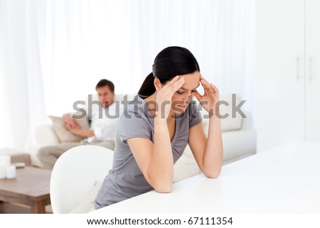 Tired woman having a headache sitting at a table in the living room with her boyfriend