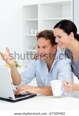 Lovely couple laughing while watching something on the laptop screen in the kitchen