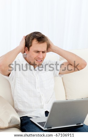 Tense man working on his laptop sitting on the sofa at home