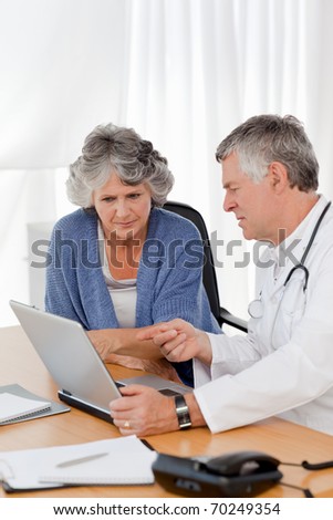 A senior doctor with his patient looking at the laptop in his office