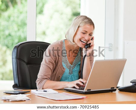 Woman working on her computer while she is phoning at home