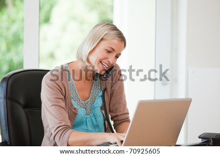 Woman working on her computer while she is phoning at home