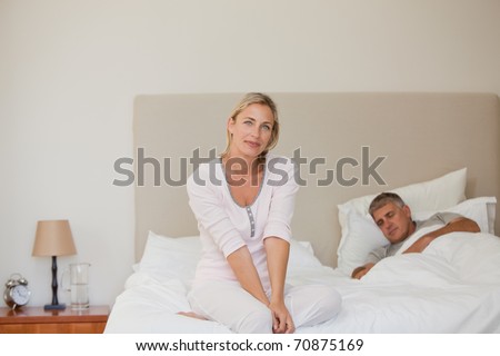 Woman looking at the camera while her husband is sleeping