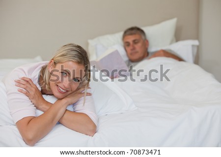 Pretty woman looking at the camera while her husband is sleeping