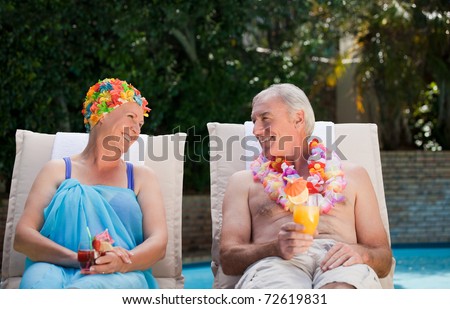 Mature couple drinking a cocktail  beside the swimming pool at home