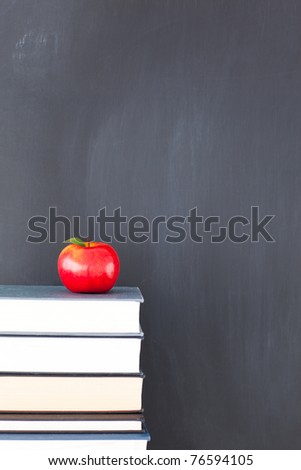Stack of books with red apple and clean blackboard