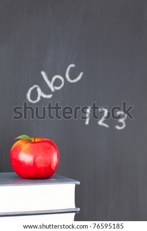 Stack of books with a red apple and a blackboard with figures and letters written on it