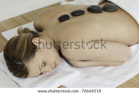 Lovely blond-haired woman lying down with stones on her back in a spa centre