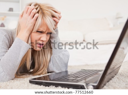 Attractive blond woman frustrated with her computer lying on a carpet in the living room
