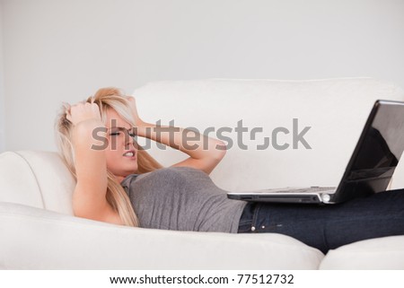 Attractive blond woman frustrated with her computer lying on a sofa in a studio