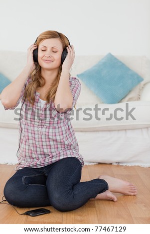 Attractive blond-haired woman listening to music with headphones in the living-room
