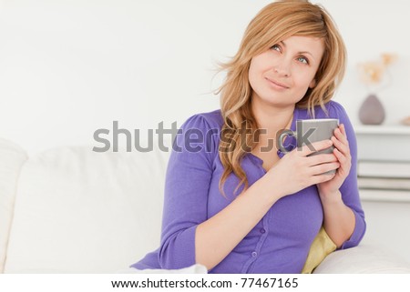 Pretty red-haired woman holding a cup of coffee while sitting on a sofa in the living room
