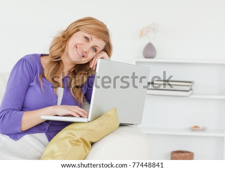 Smiling happy woman sitting on the sofa and using a laptop in her apartment