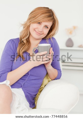 Good looking red-haired woman holding a cup of coffee while sitting on a sofa in the living room