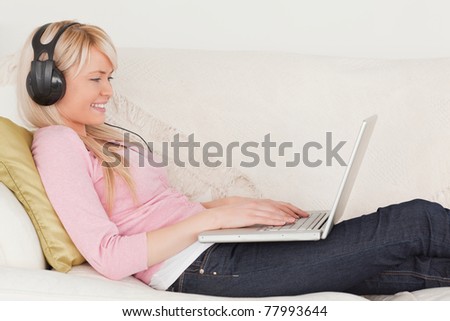Good looking female listening to music on her headphones while lying on a sofa in the living room
