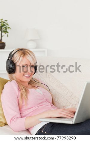 Pretty female listening to music on her headphones while lying on a sofa in the living room