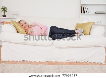 Attractive blonde woman watching tv while lying on a sofa in the living room