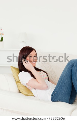 Attractive red-haired woman having a conversation on the phone while lying on a sofa in the living room