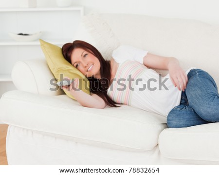 Charming red-haired woman watching tv while lying on a sofa in the living room