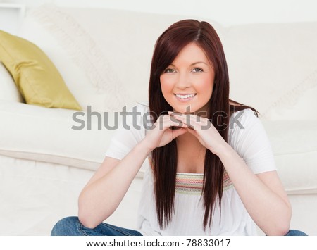Good looking red-haired woman posing while sitting on a carpet in the living room