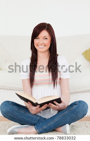 Good looking red-haired woman reading a book while sitting on a sofa in the living room