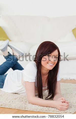 Good looking red-haired woman posing while lying on a carpet in the living room