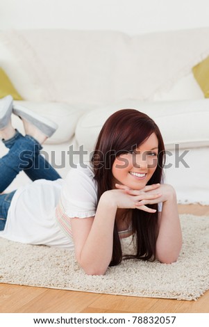 Cute red-haired woman posing while lying on a carpet in the living room