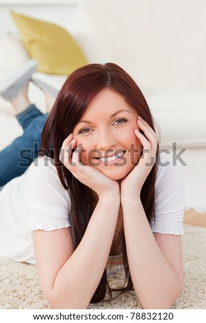 Happy red-haired woman posing while lying on a carpet in the living room