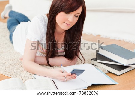Good looking red-haired female studying for while lying on a carpet in the living room