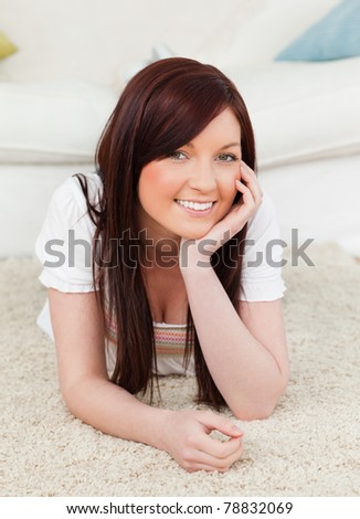 Happy red-haired female posing while lying on a carpet in the living room