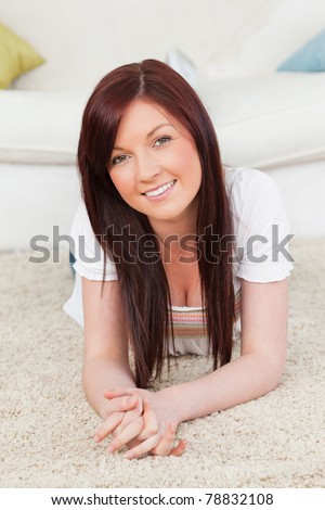 Good looking red-haired female posing while lying on a carpet in the living room