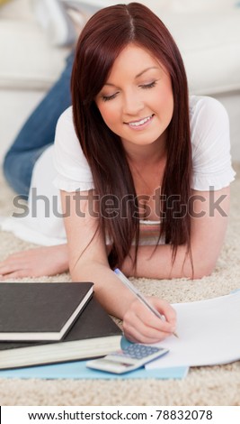 Charming red-haired female studying for while lying on a carpet in the living room