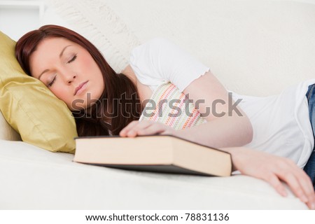 Beautiful red-haired girl having a rest while studying on a sofa in the living room