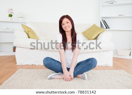 Good looking red-haired female posing while sitting on a carpet in the living room