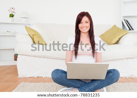 Attractive female relaxing with her laptop while siting on a carpet in the living room