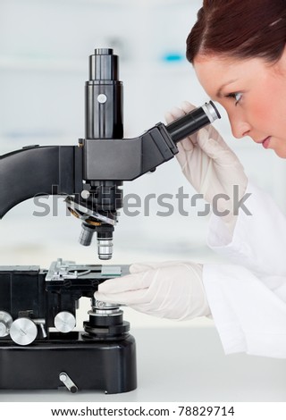 Beautiful red-haired scientist looking through a microscope in a lab