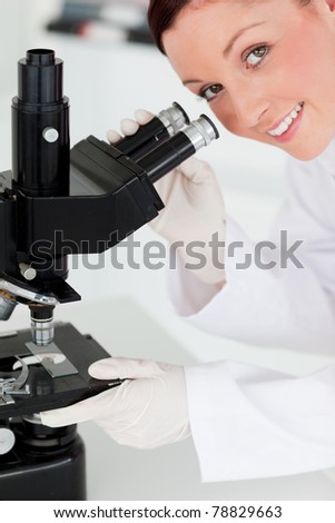 Charming red-haired scientist looking through a microscope in a lab