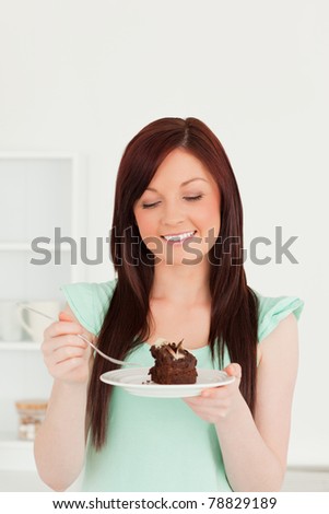 Attractive red-haired woman eating some cake in the kitchen in her apartment